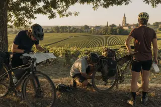 Cyclists pausing by a vineyard near Saint-Émilion, repairing a bike and checking a map at sunset, with bikes loaded for touring.